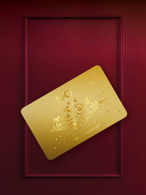 Una carta dorata con un motivo ornato e le lettere "K&O" è posizionata in diagonale su uno sfondo rosso vinaccia con cornice rettangolare.
