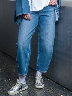Una persona che indossa jeans blu, una giacca di jeans, calzini bianchi e scarpe da ginnastica grigie è in piedi in una casa accanto a una superficie metallica.