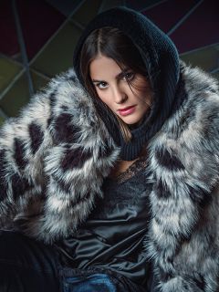 Una persona che indossa un passamontagna nero con cappuccio e un cappotto di pelliccia sintetica fantasia sopra un top nero bordato di pizzo.